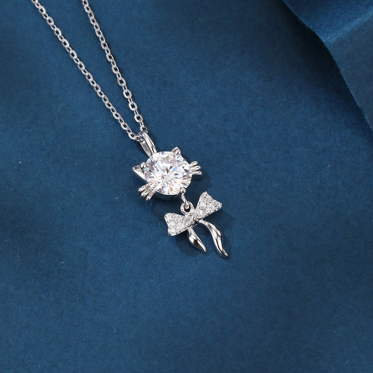 Elegant silver necklace with round diamond pendant and sparkling bow charm on blue velvet