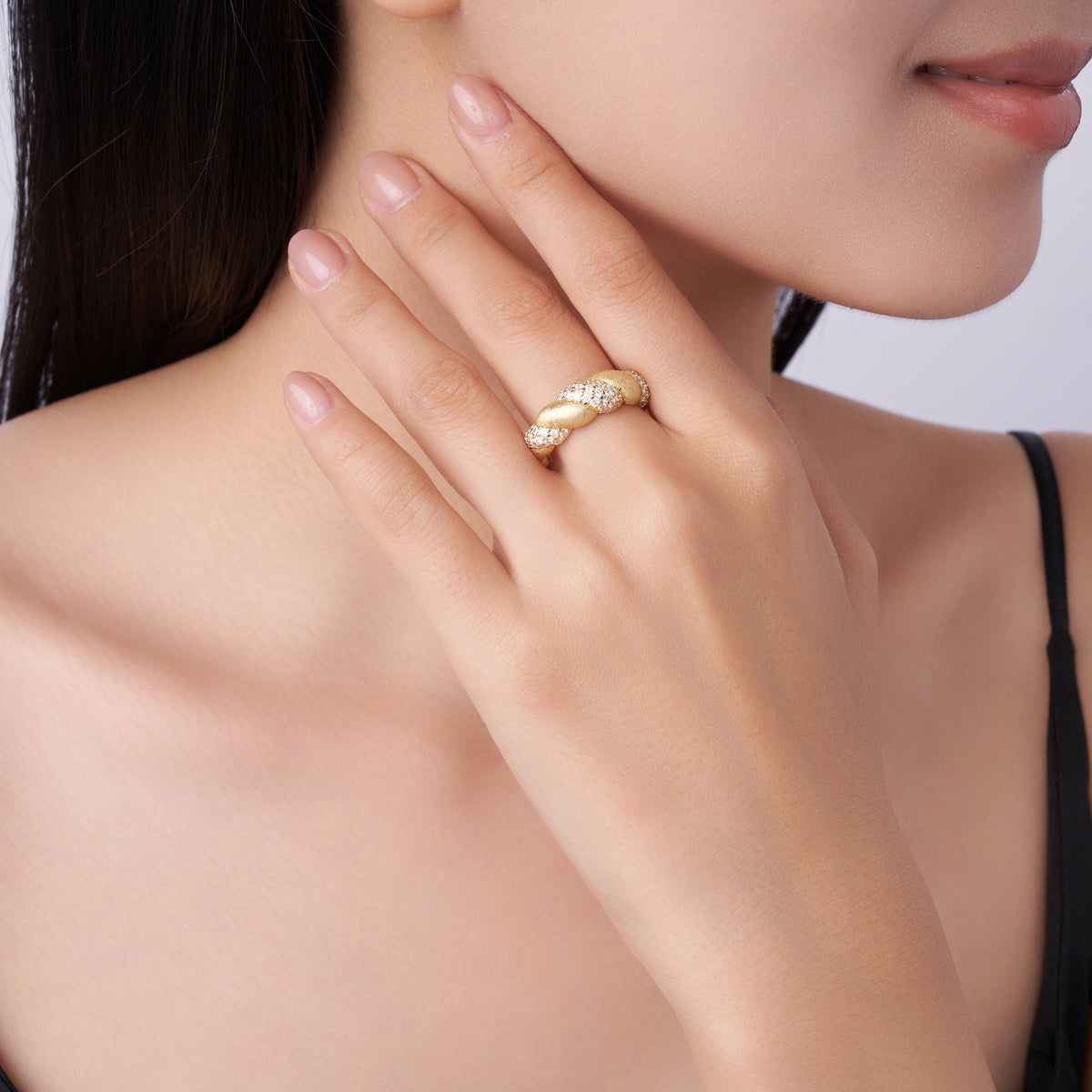 Gold twisted ring with pavé diamonds on woman’s hand, minimalist luxury jewelry design