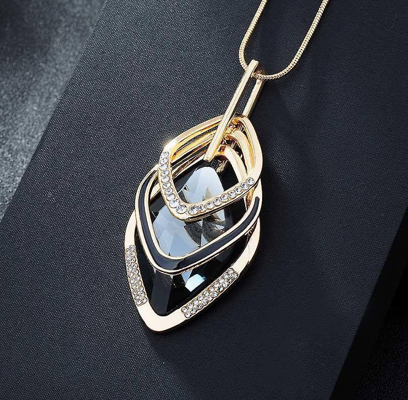 Luxury gold pendant with black enamel and crystal accents, minimalist design on dark fabric