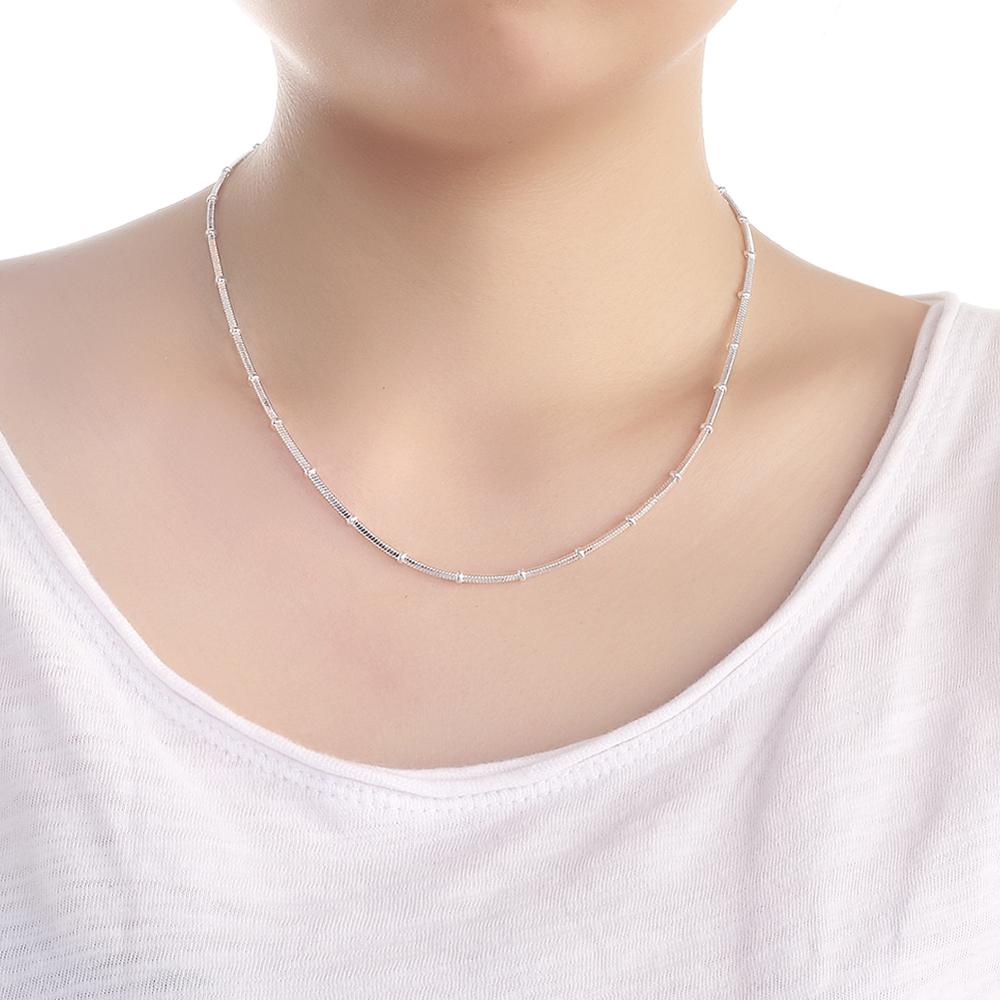 Minimalist silver chain necklace with textured links, worn on a model in a white top