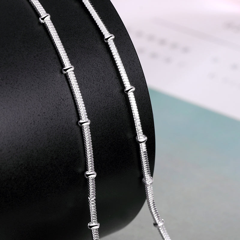 Minimalist silver snake chain necklace with sleek links, displayed on black stand for luxury jewelry collection