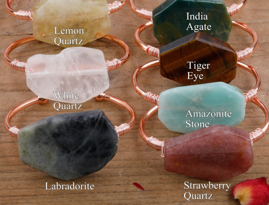 Handcrafted gemstone rings in Lemon Quartz, Tiger Eye, Amazonite, and more, set in copper wire on wood.