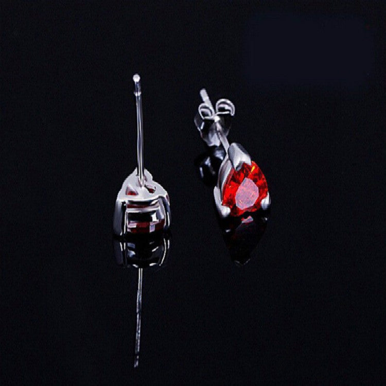 Luxury red gemstone stud earrings with minimalist silver setting, reflecting on black surface