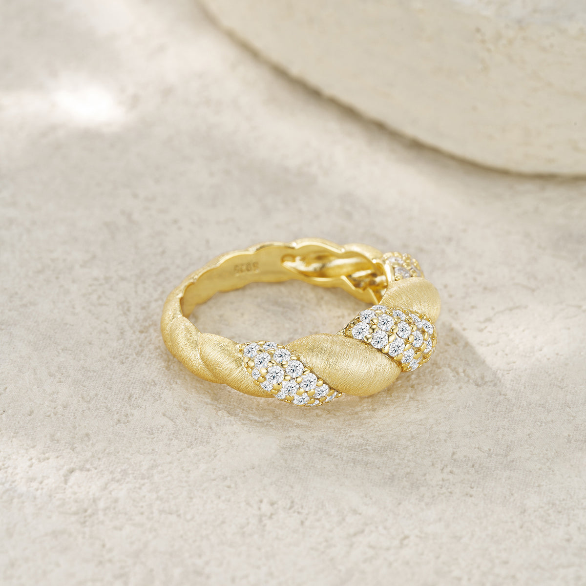Luxury gold ring with twisted design and sparkling diamond accents on textured surface