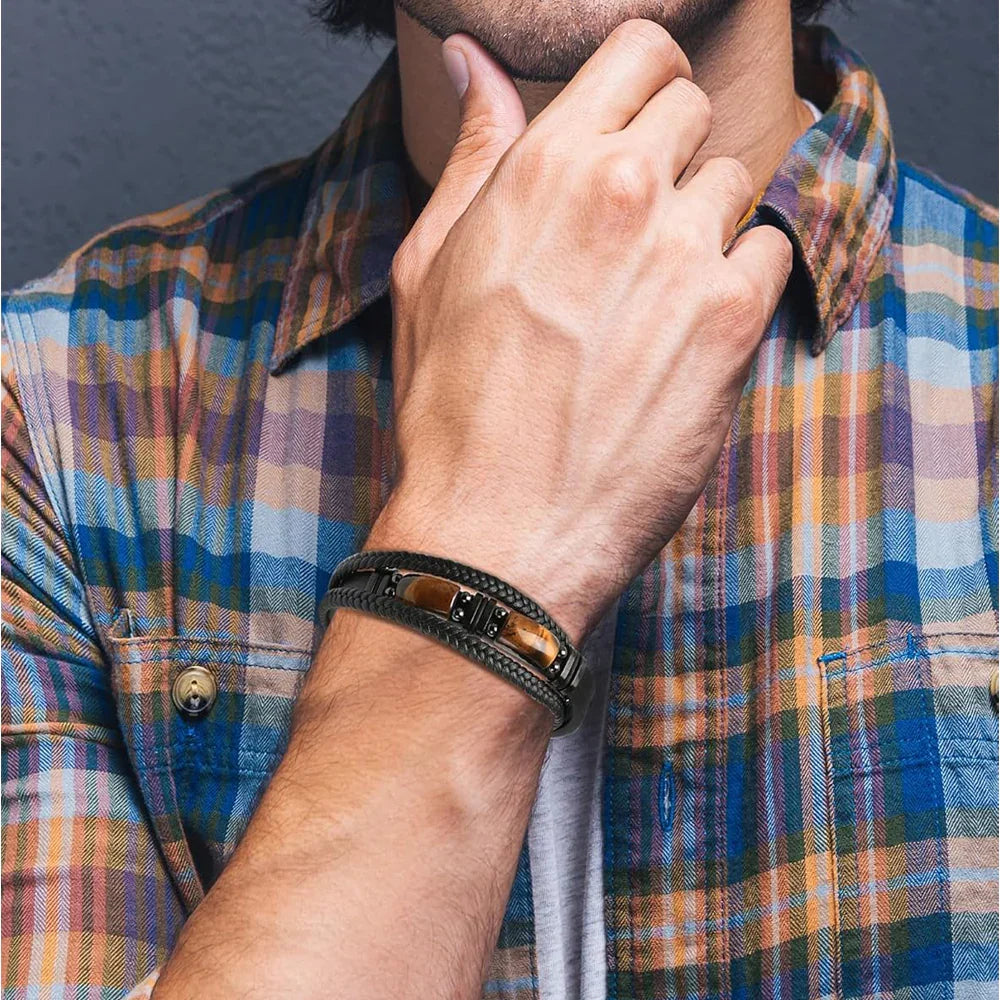 Men's braided leather bracelet with tiger eye stone, worn with plaid shirt for casual luxury style.