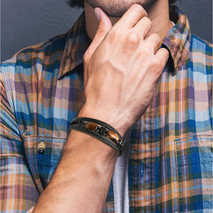 Men's braided leather bracelet with tiger eye stone, worn with plaid shirt for casual luxury style.