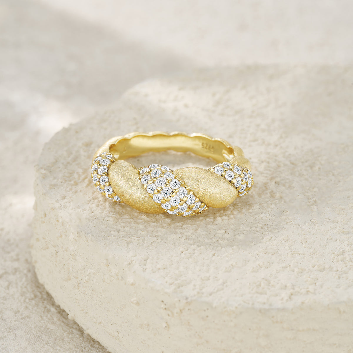 Luxury gold ring with twisted design and pavé diamonds on textured stone