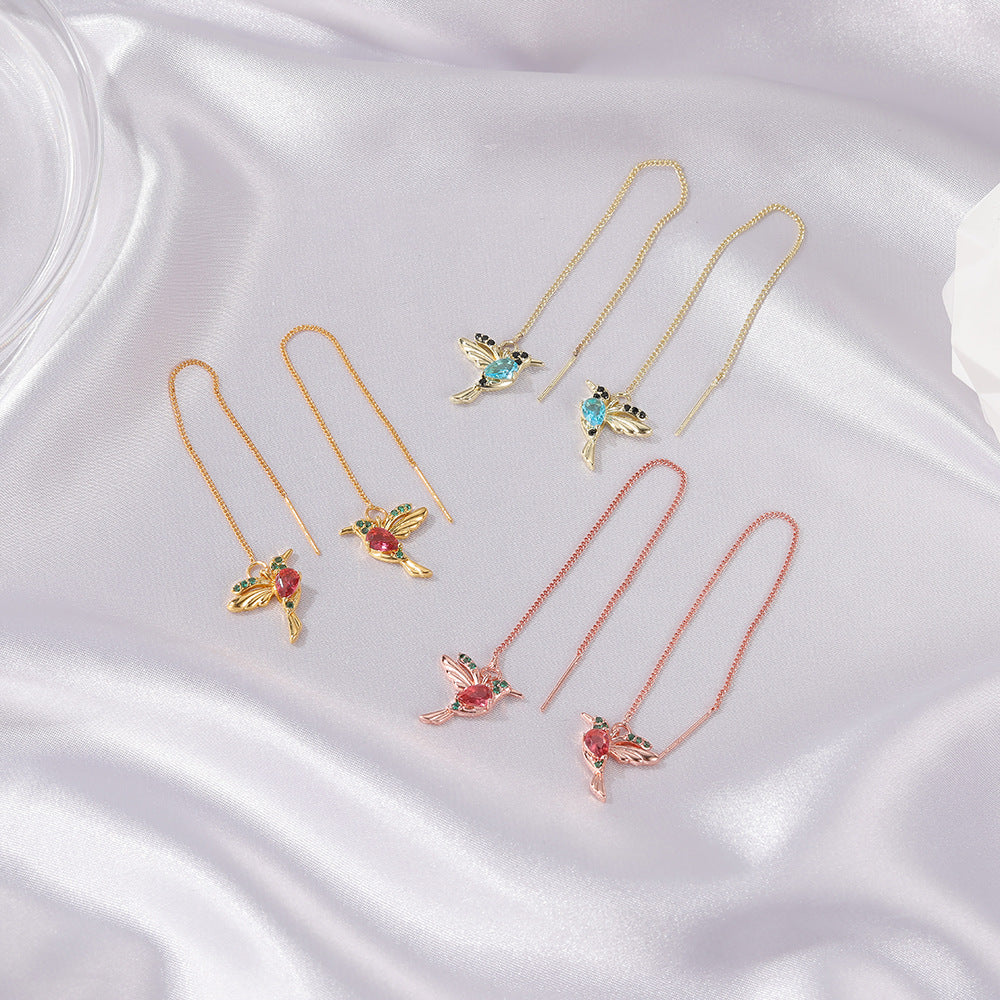 Delicate hummingbird threader earrings with gemstone accents, gold and rose gold tones on satin