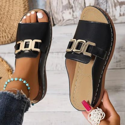 Black leather slide sandals with gold buckle, worn with denim, showcasing minimalist luxury footwear design
